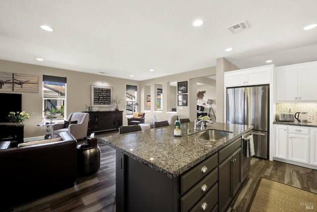 kitchen featuring a sink, dark stone counters, open floor plan, visible vents, and freestanding refrigerator