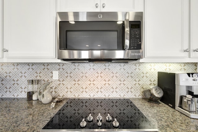 kitchen with white cabinets, backsplash, stainless steel microwave, stone counters, and black electric stovetop