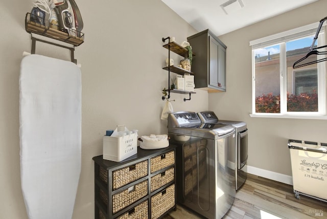 washroom featuring light wood-style flooring, baseboards, visible vents, separate washer and dryer, and cabinet space