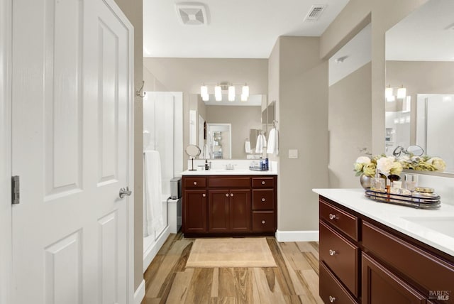 full bathroom with two vanities, a stall shower, baseboards, visible vents, and wood finished floors