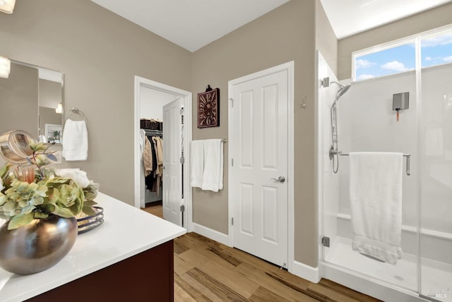bathroom with baseboards, a spacious closet, wood finished floors, a shower stall, and vanity