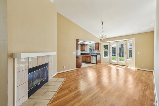 unfurnished living room with lofted ceiling, light wood-type flooring, baseboards, a notable chandelier, and a fireplace