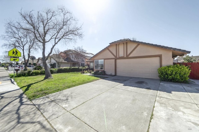 tudor house with stucco siding, fence, driveway, a front yard, and a garage