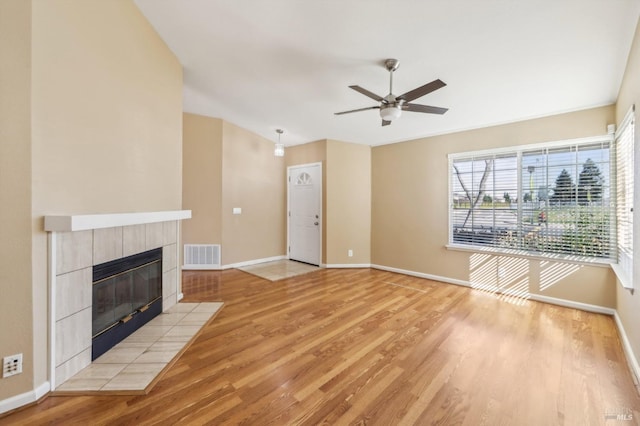 unfurnished living room featuring baseboards, visible vents, light wood-style flooring, a tile fireplace, and ceiling fan