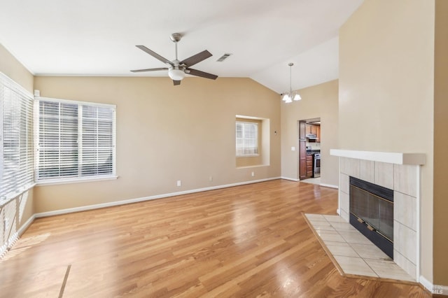 unfurnished living room featuring a tile fireplace, light wood finished floors, baseboards, lofted ceiling, and ceiling fan with notable chandelier