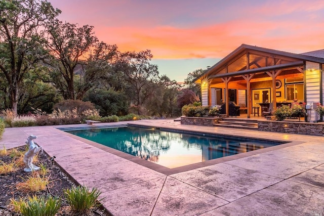 pool at dusk with a diving board, an outdoor pool, and a patio