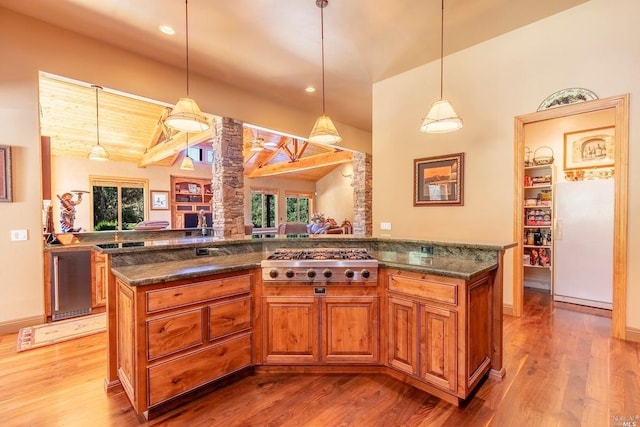 kitchen with stainless steel gas cooktop, light wood-type flooring, decorative columns, vaulted ceiling with beams, and brown cabinetry