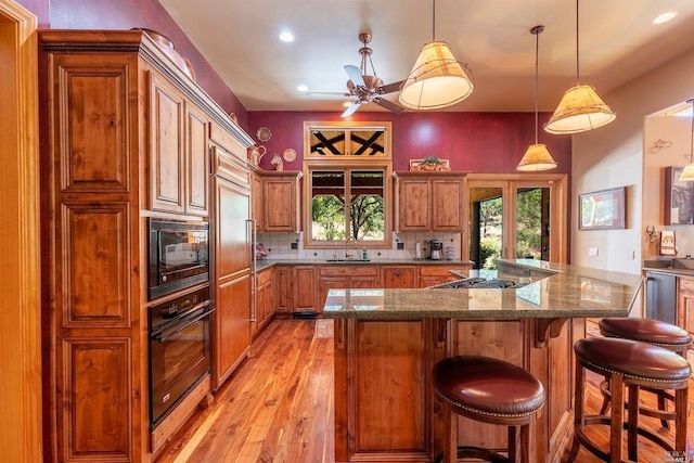 kitchen with light wood finished floors, a ceiling fan, tasteful backsplash, black appliances, and brown cabinetry
