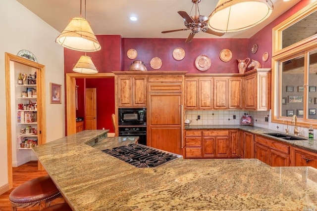 kitchen with light stone counters, a sink, a ceiling fan, black appliances, and decorative backsplash