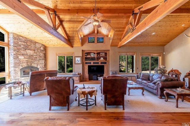 living area with a healthy amount of sunlight, a fireplace, beamed ceiling, and a ceiling fan