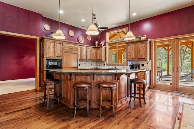 kitchen featuring backsplash, wood finished floors, black microwave, and brown cabinets