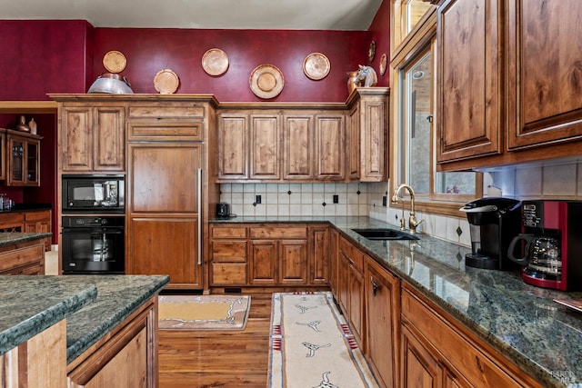 kitchen with a sink, brown cabinetry, dark stone countertops, black appliances, and decorative backsplash