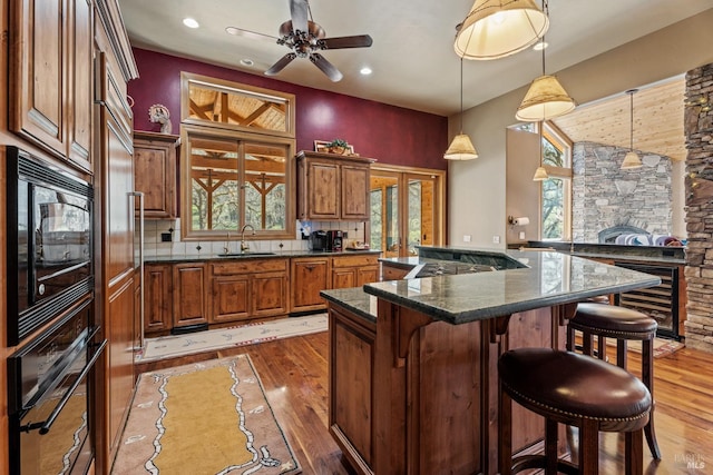 kitchen with a kitchen breakfast bar, light wood-style flooring, a sink, and black appliances