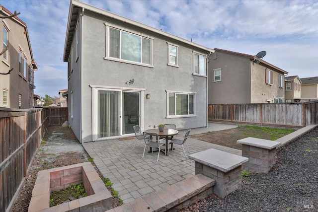 rear view of house with stucco siding, a fenced backyard, and a patio area