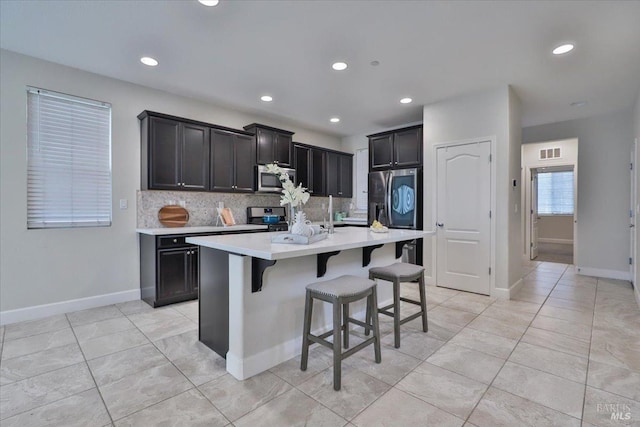 kitchen with light countertops, a breakfast bar, stainless steel appliances, visible vents, and decorative backsplash