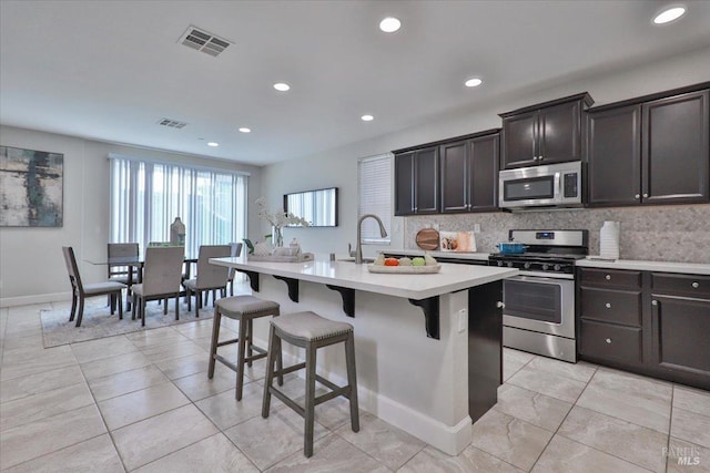kitchen featuring an island with sink, light countertops, backsplash, a kitchen breakfast bar, and stainless steel appliances