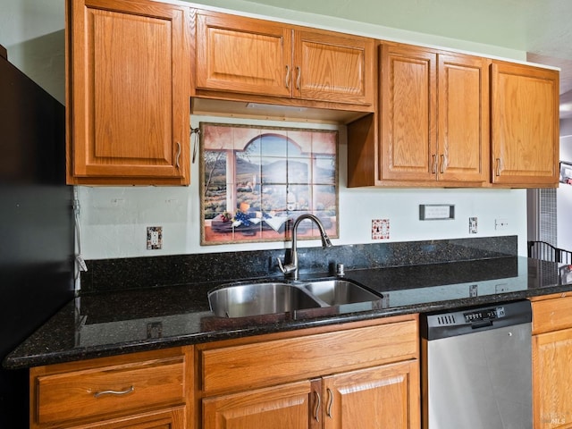 kitchen with dark stone counters, freestanding refrigerator, brown cabinetry, dishwasher, and a sink