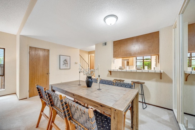 dining room featuring stairs, light colored carpet, baseboards, a textured ceiling, and visible vents