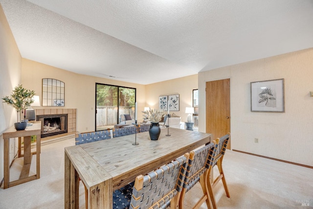 dining area with baseboards, a textured ceiling, a tiled fireplace, and light carpet