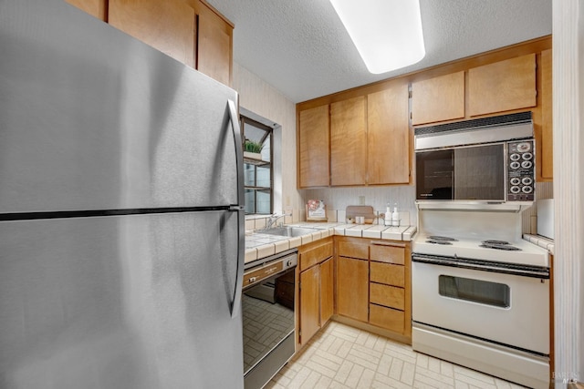 kitchen with a textured ceiling, dishwasher, a sink, freestanding refrigerator, and electric range