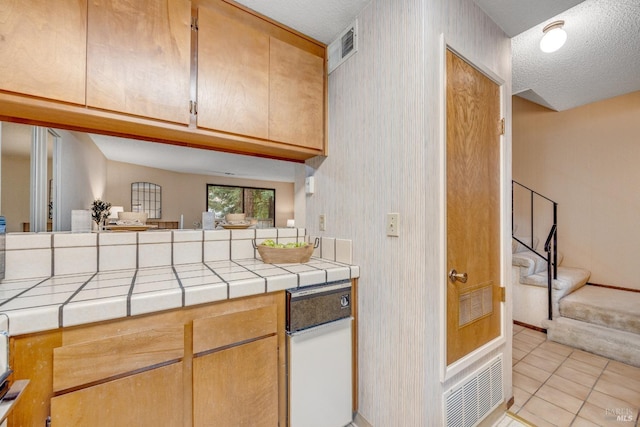 kitchen with a textured ceiling, tile countertops, visible vents, and light tile patterned floors
