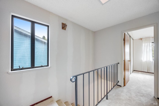 hall featuring a textured ceiling, carpet flooring, and an upstairs landing