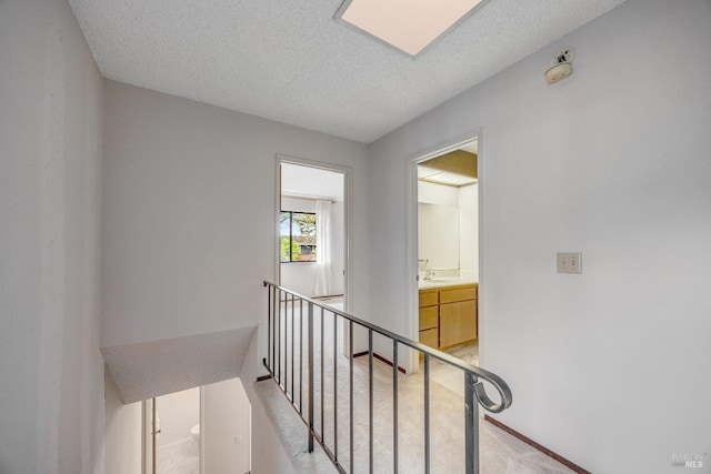 hall with an upstairs landing, a skylight, light colored carpet, and a textured ceiling