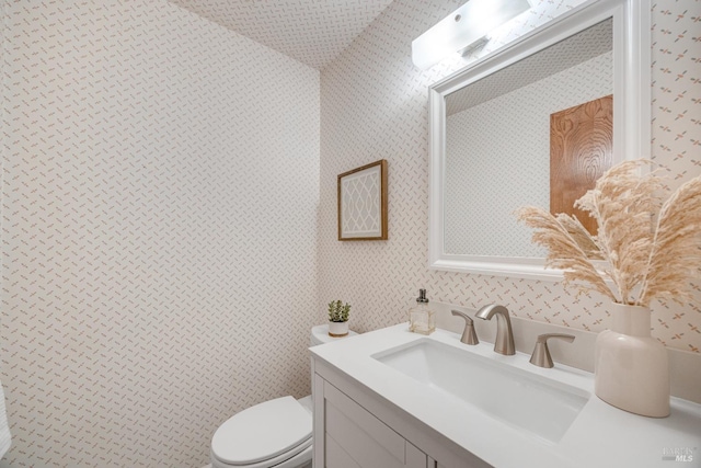half bath featuring wallpapered walls, toilet, and vanity
