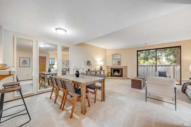 dining area with light carpet, a tile fireplace, and a textured ceiling