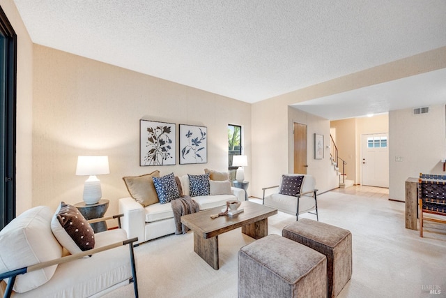 living area featuring a textured ceiling, visible vents, stairway, and light colored carpet