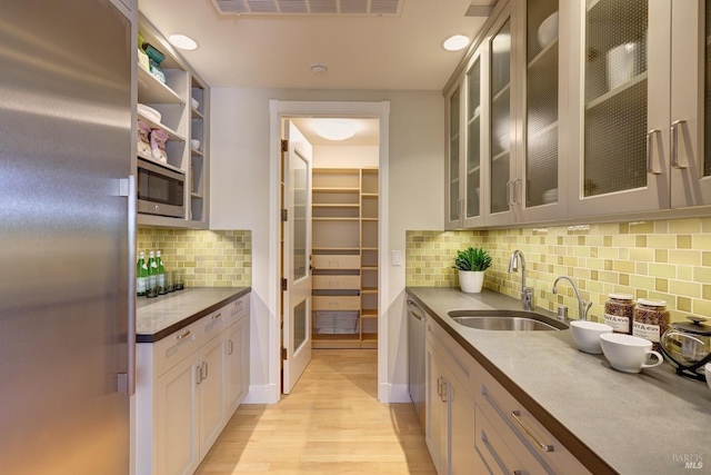 kitchen featuring a sink, stainless steel appliances, tasteful backsplash, light wood-type flooring, and glass insert cabinets
