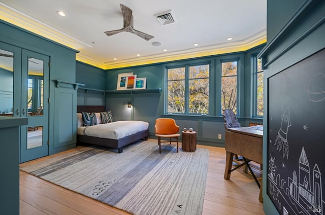 bedroom with crown molding, hardwood / wood-style floors, visible vents, and a decorative wall
