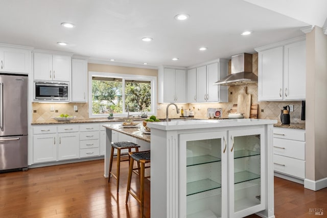 kitchen featuring a breakfast bar, wall chimney exhaust hood, stainless steel appliances, and light wood-style floors