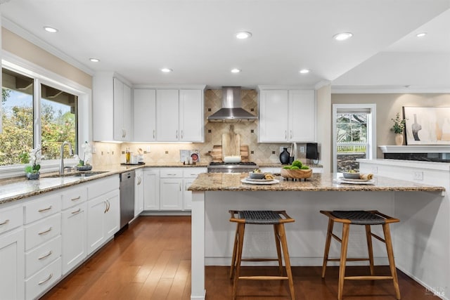 kitchen with dishwasher, a sink, a healthy amount of sunlight, a breakfast bar area, and wall chimney range hood