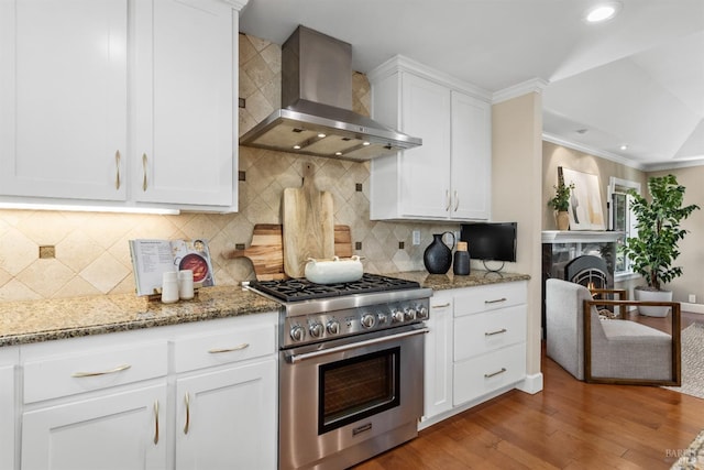 kitchen featuring white cabinets, crown molding, wood finished floors, wall chimney exhaust hood, and high end stainless steel range oven