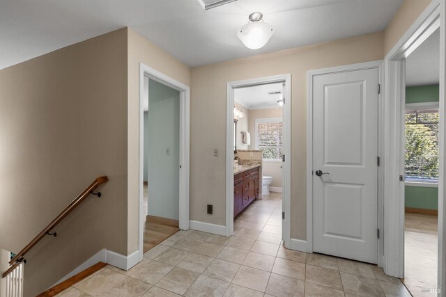 corridor with light tile patterned flooring, an upstairs landing, and baseboards