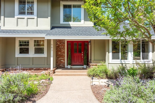 view of exterior entry featuring stucco siding, a shingled roof, and brick siding