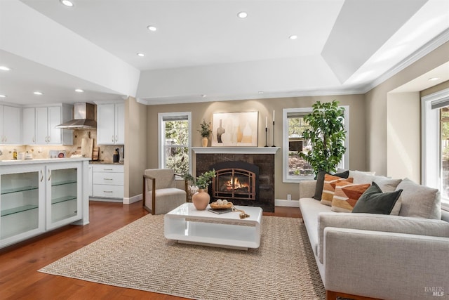 living room with recessed lighting, ornamental molding, a raised ceiling, a high end fireplace, and wood finished floors