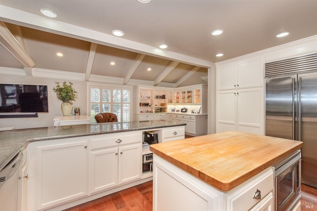 kitchen featuring butcher block countertops, wood finished floors, a kitchen island, white cabinetry, and built in appliances
