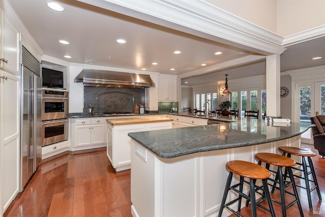 kitchen featuring stainless steel appliances, dark wood-style floors, a large island, and wall chimney exhaust hood