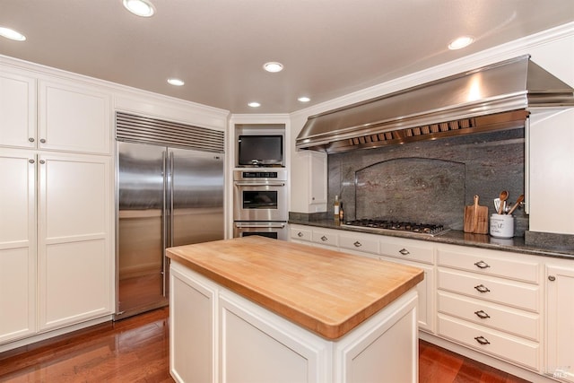 kitchen with a kitchen island, appliances with stainless steel finishes, butcher block counters, custom exhaust hood, and dark wood-type flooring