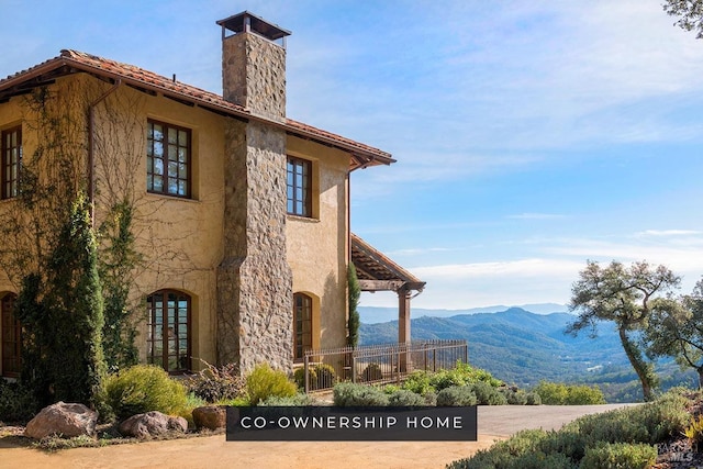 view of property exterior featuring a tiled roof, a mountain view, stucco siding, and a chimney