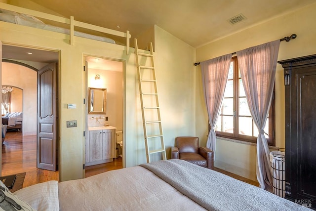 bedroom featuring arched walkways, visible vents, and wood finished floors