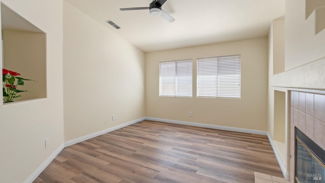 unfurnished living room with visible vents, baseboards, wood finished floors, a tiled fireplace, and a ceiling fan