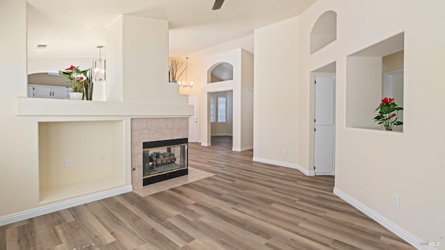 unfurnished living room with baseboards, wood finished floors, a tiled fireplace, and a ceiling fan