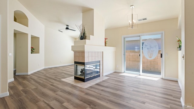 unfurnished living room featuring visible vents, baseboards, wood finished floors, a tiled fireplace, and ceiling fan with notable chandelier