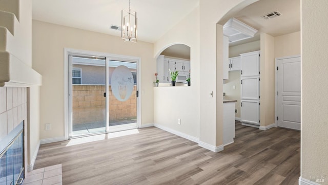 unfurnished dining area with wood finished floors, arched walkways, a chandelier, and visible vents