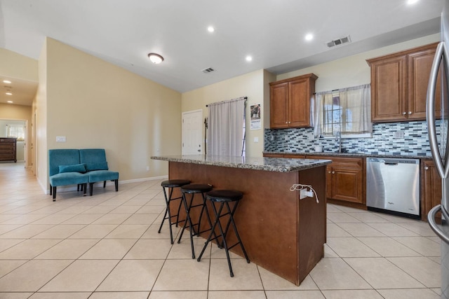 19810 S Spruce Rd, Los Banos, CA 93635 - kitchen with appliances with stainless steel finishes, a kitchen island, a breakfast bar area, decorative backsplash, and light tile patterned floors