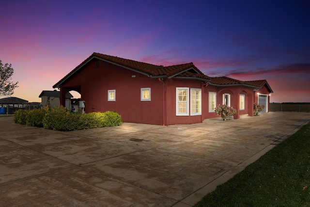 19810 S Spruce Rd, Los Banos, CA 93635 - property exterior at dusk with concrete driveway, a tile roof, an attached garage, and stucco siding