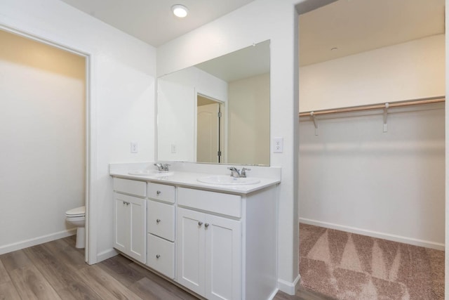 bathroom with baseboards, double vanity, a sink, and toilet